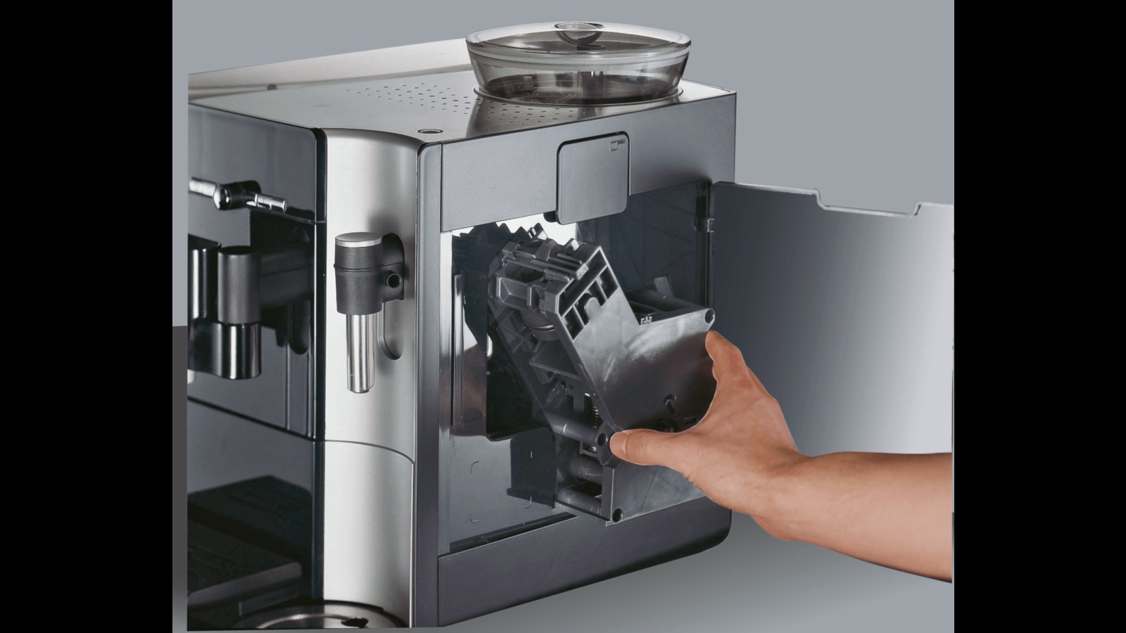 Czyszczenie lub naprawa automatycznego ekspresu do kawy: dłoń wyjmuje pojemnik na fusy z wnętrza urządzenia.