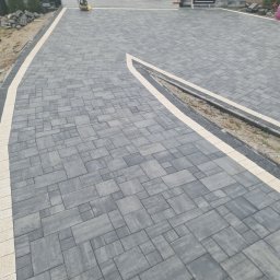 HKS- INFRASTRUKTURA Sławomir Hebda - Ułożona szara kostka brukowa z jasnymi obrzeżami, tworząca wzór na podjeździe. Widoczny fragment odwodnienia liniowego i przygotowane materiały budowlane.