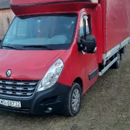 Czerwony samochód dostawczy Renault Master z plandeką i nadbudówką sypialną, zaparkowany na trawiastym podłożu, widoczne ślady opon.