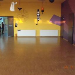 Ecologi Investment - Pusta sala z żółtymi ścianami udekorowana na Halloween, widoczne dekoracje: duch, pająk, szkielet w cylindrze, pod ścianami zamontowane białe grzejniki, podłoga parkietowa