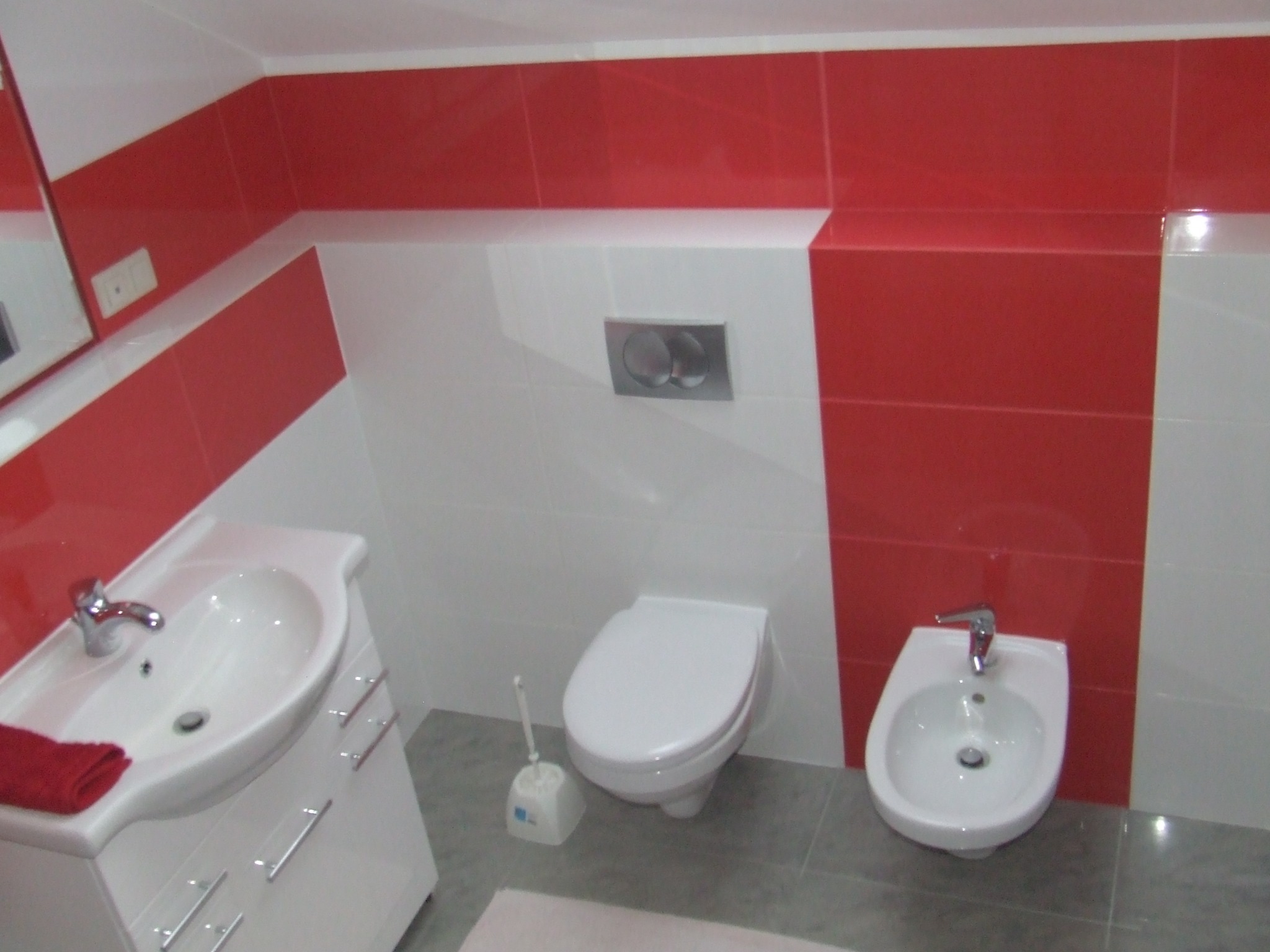 Nowoczesna łazienka z czerwono-białymi płytkami, umywalką z szafką, toaletą podwieszaną i bidetem.