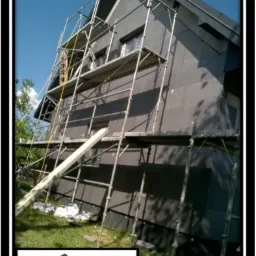 Dom jednorodzinny w trakcie ocieplania, widoczne rusztowania i grafitowe płyty termoizolacyjne na ścianach, w dolnym rogu logo firmy remontowo-budowlanej.