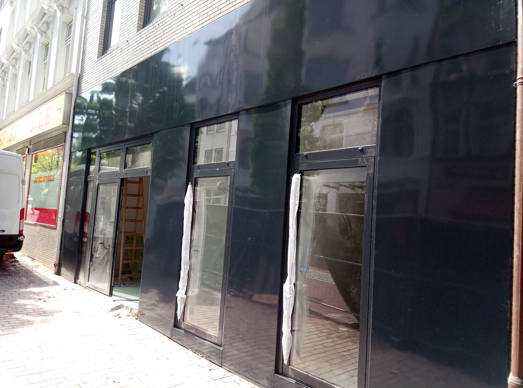 Nowe, czarne okna wystawowe z folią ochronną w trakcie montażu w lokalu usługowym, widoczna drabina wewnątrz.