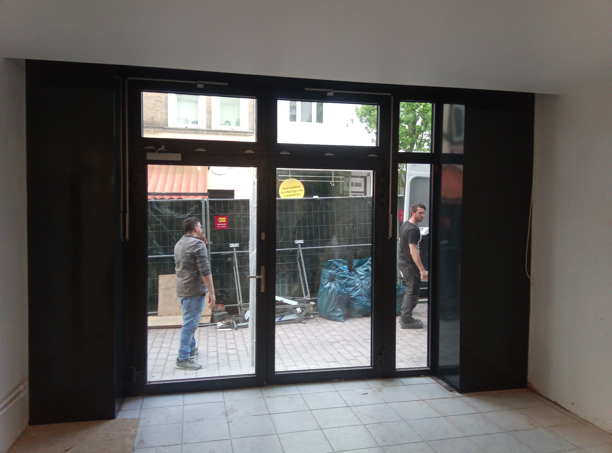 Montaż czarnych drzwi przesuwnych z widocznymi pracownikami w trakcie instalacji na zewnątrz budynku z widocznymi workami z odpadami budowlanymi.