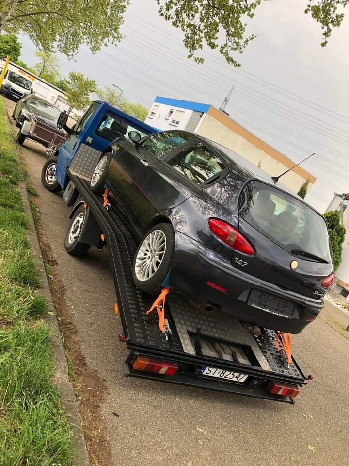 Alfa Romeo 147 zabezpieczona pasami na lawecie w Westheim, gotowa do transportu. Widoczny numer rejestracyjny pojazdu.
