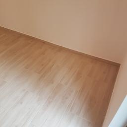 Usługi remontowo budowlane - Ukończona podłoga z płytek imitujących drewno w rogu pomieszczenia, z listwą przypodłogową, widok z góry pod kątem.