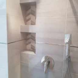 Wykończona ściana prysznicowa z wnękami wyłożonymi mozaiką w jodełkę, bateria i słuchawka prysznicowa.