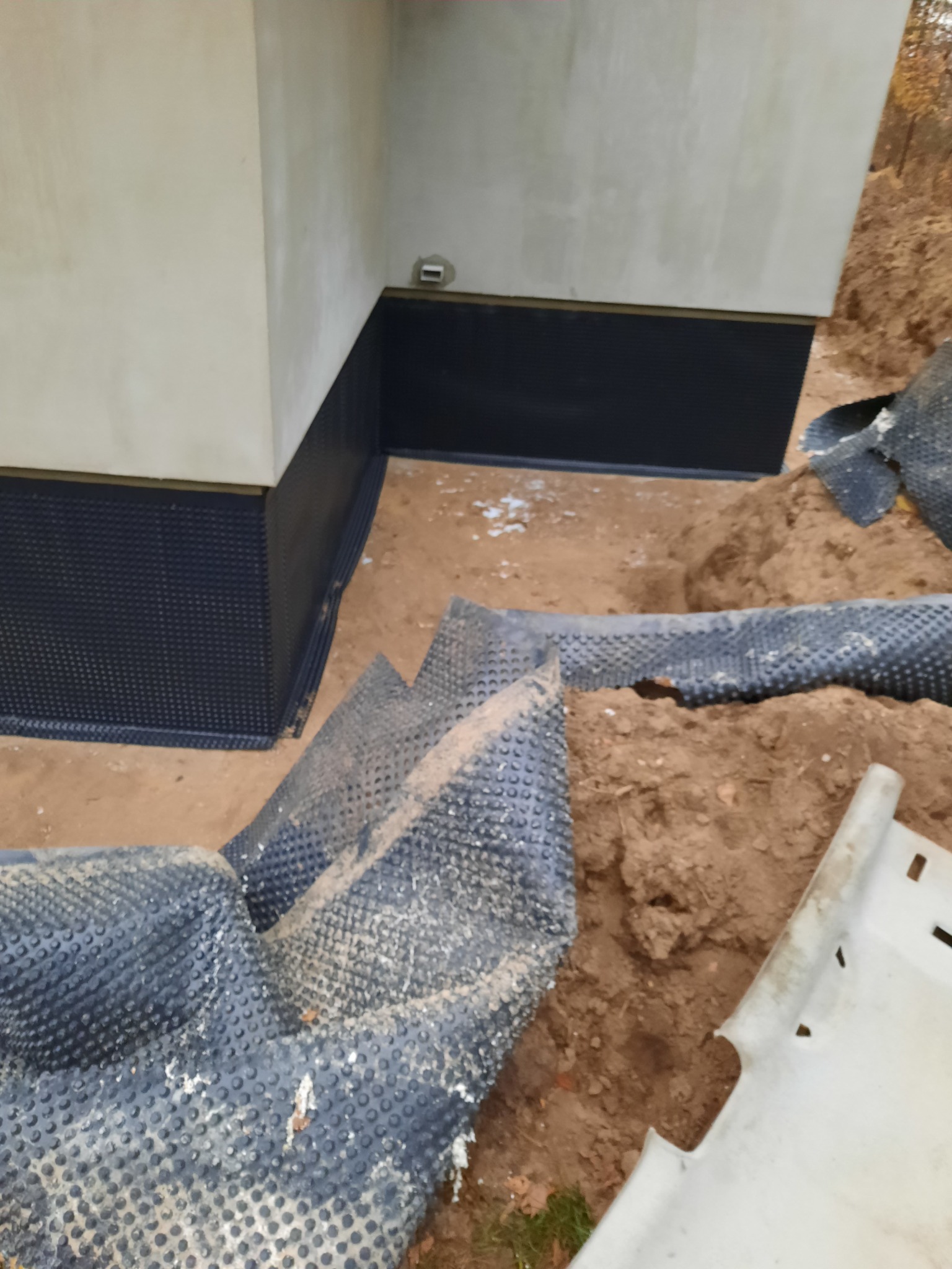 Fundament budynku z nałożoną izolacją pionową, widoczne fragmenty folii kubełkowej w wykopie.