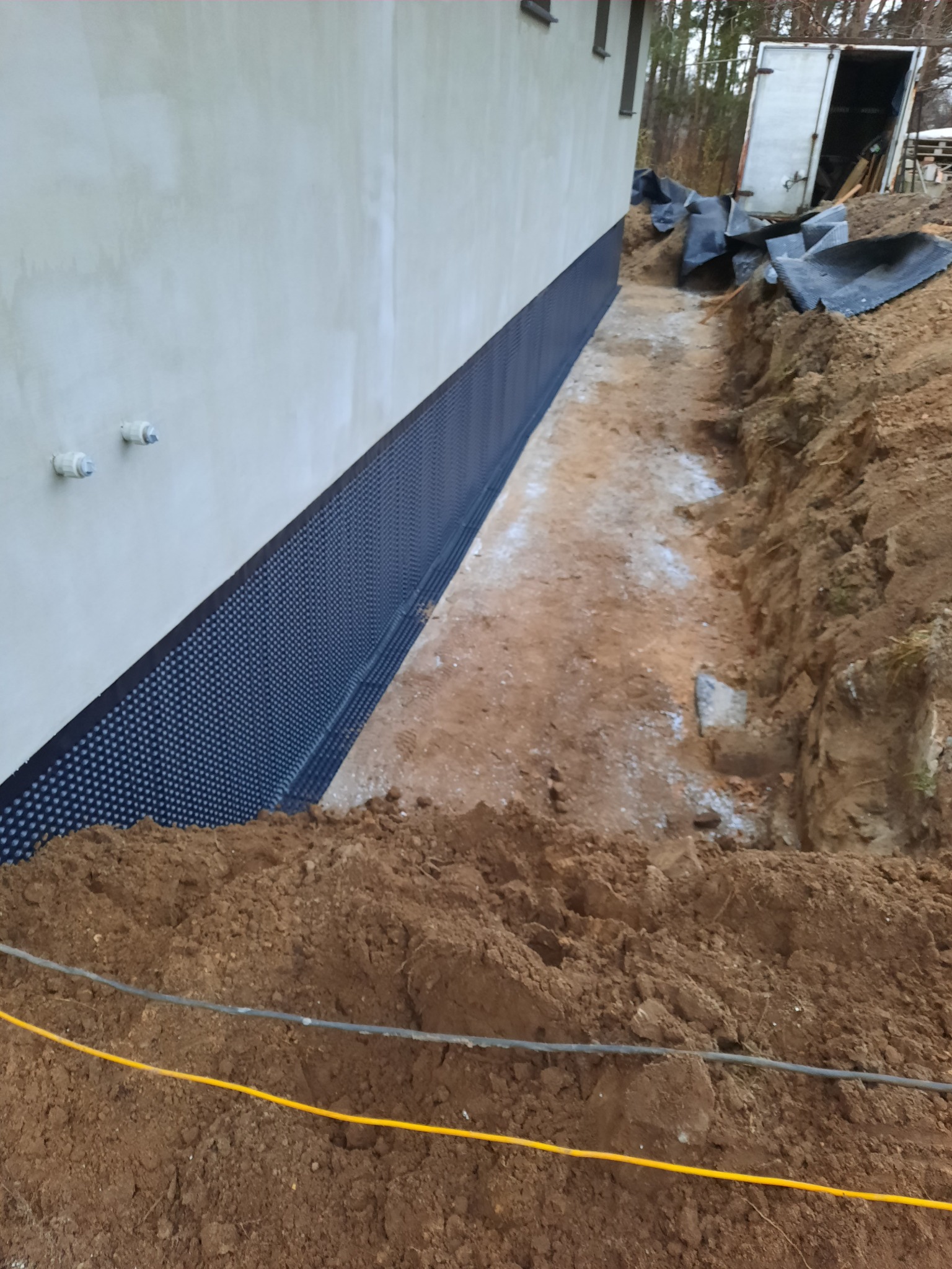 Fundament budynku zabezpieczony folią kubełkową, wykop wokół fundamentu, widoczne przewody elektryczne w ziemi.