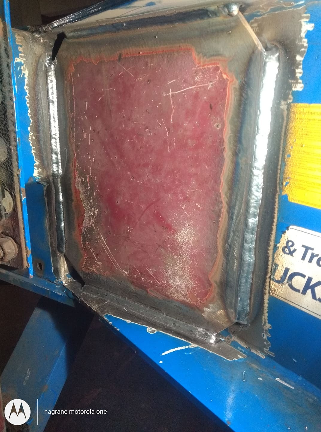 Spoina spawalnicza na konstrukcji stalowej, widoczne ślady szlifowania i pozostałości po spawaniu, niebieska farba na elementach konstrukcyjnych.