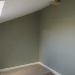 Pomalowane na oliwkowy kolor wnętrze poddasza ze skosami, widoczne listwy przypodłogowe i fragment okna dachowego.