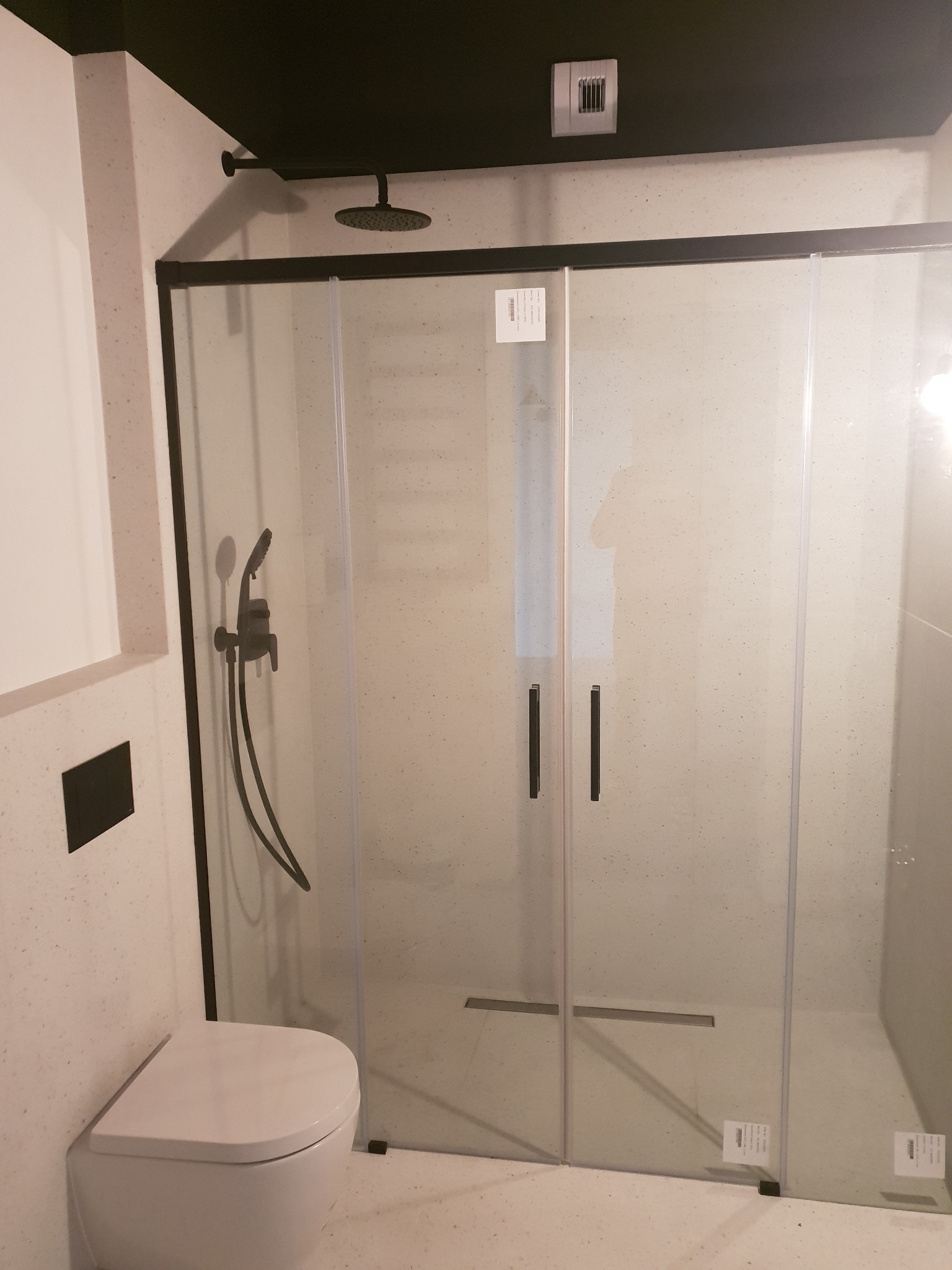 Nowoczesna łazienka z kabiną prysznicową z czarnymi ramami, deszczownicą i baterią podtynkową, wisząca toaleta oraz ciemny sufit.