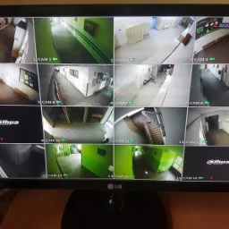 Monitor wyświetlający obraz z szesnastu kamer monitoringu wizyjnego, prezentujący widok korytarzy i schodów w budynku. Na ekranie widoczne daty i oznaczenia kamer.