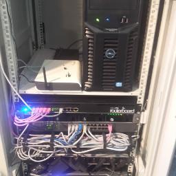 Serwis1 Adam Zdybel - Szafa rack z serwerem Dell, routerem MikroTik Routerboard, switchem i punktem dostępowym Wi-Fi, okablowanie strukturalne z różowymi kablami Ethernet.
