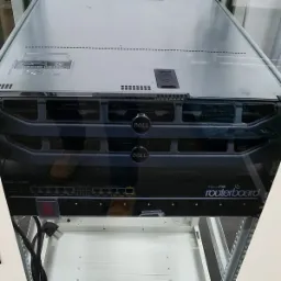 Zamontowany w szafie serwer Dell PowerEdge R320 i routerboard MikroTik, widoczne porty Ethernet i kable zasilające.