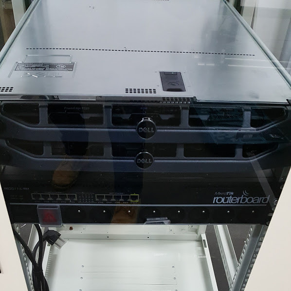 Zamontowany w szafie serwer Dell PowerEdge R320 i routerboard MikroTik, widoczne porty Ethernet i kable zasilające.