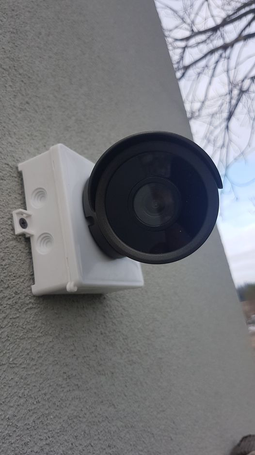 Zewnętrzna kamera monitoringu przymocowana do ściany budynku, widoczne drzewa w tle.