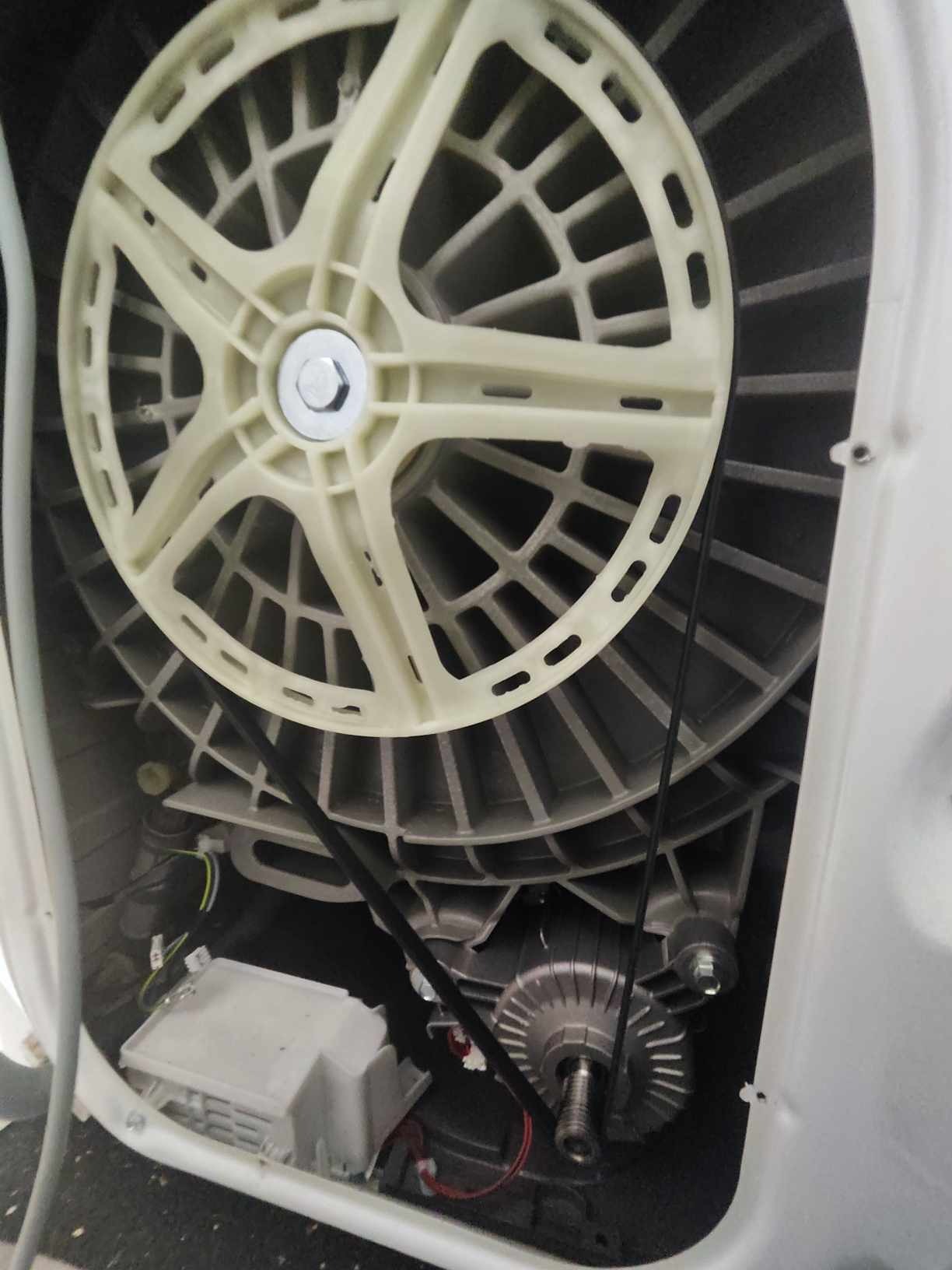 Wnętrze pralki automatycznej z widocznym bębnem, paskiem klinowym i silnikiem po zdjęciu obudowy, ukazujące elementy mechaniczne urządzenia.