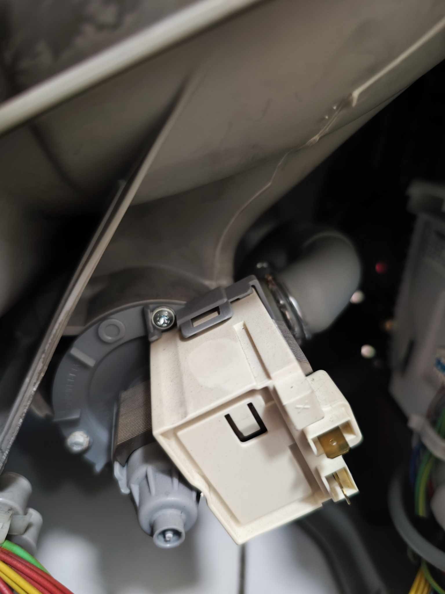 Wnętrze pralki z widoczną pompą odpływową, obudową i przewodami elektrycznymi w trakcie demontażu lub naprawy.