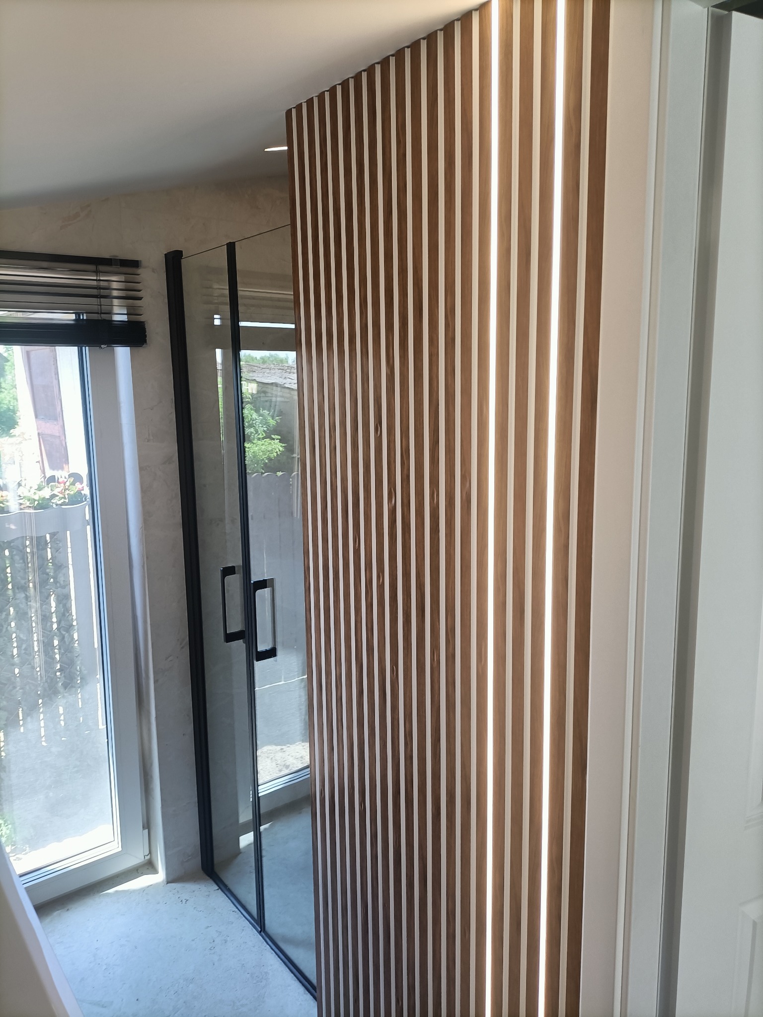 Nowoczesna kabina prysznicowa z czarnymi profilami, drewniane lamele ścienne, okno z widokiem na zieleń.