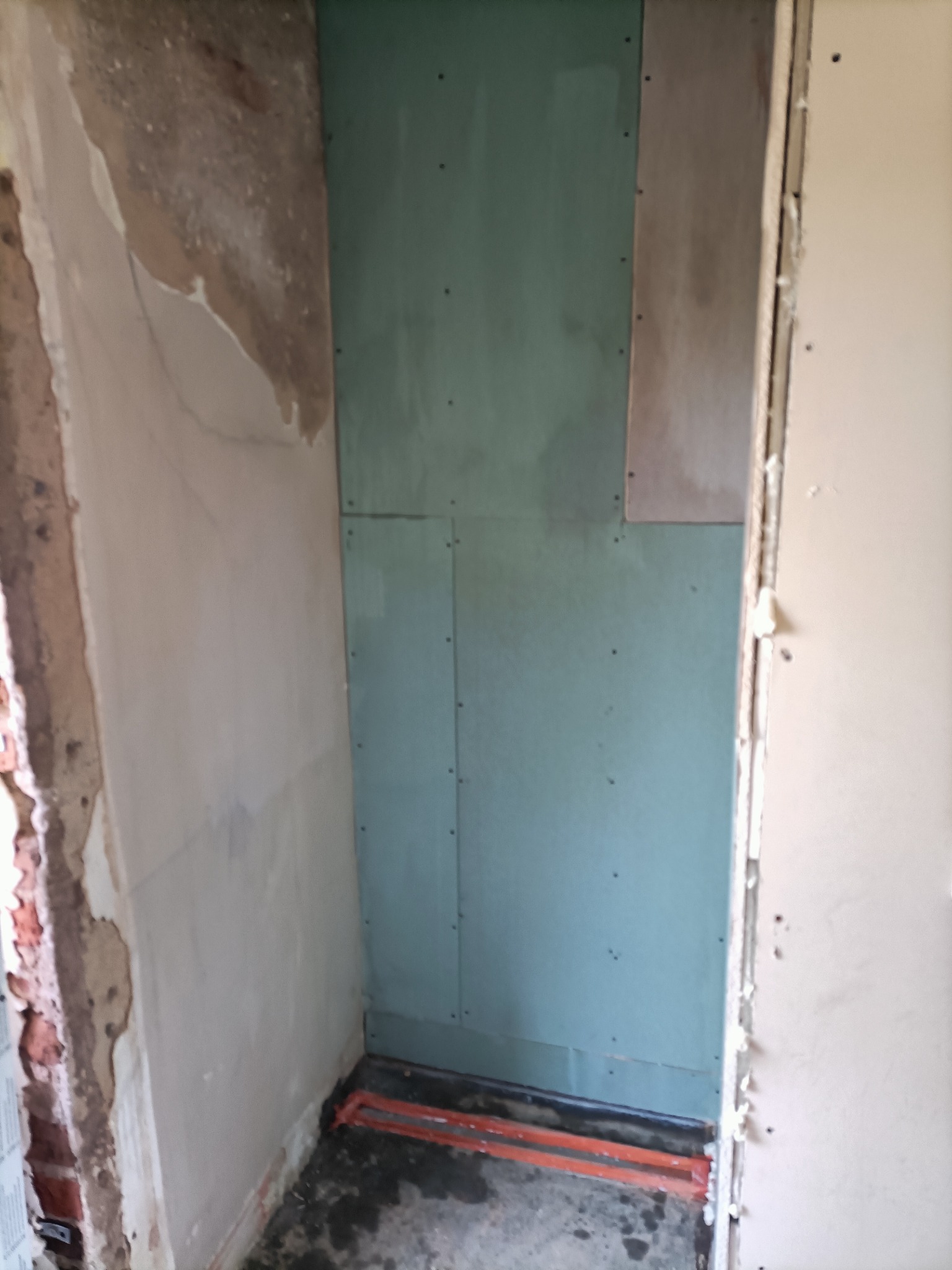 Fragment ściany z zamontowaną płytą kartonowo-gipsową w trakcie prac wykończeniowych, widoczne ślady po kleju i niedoskonałości podłoża.