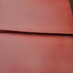 Czerwona, metalowa powierzchnia z widocznymi łączeniami paneli, prawdopodobnie po procesie czyszczenia lub malowania.