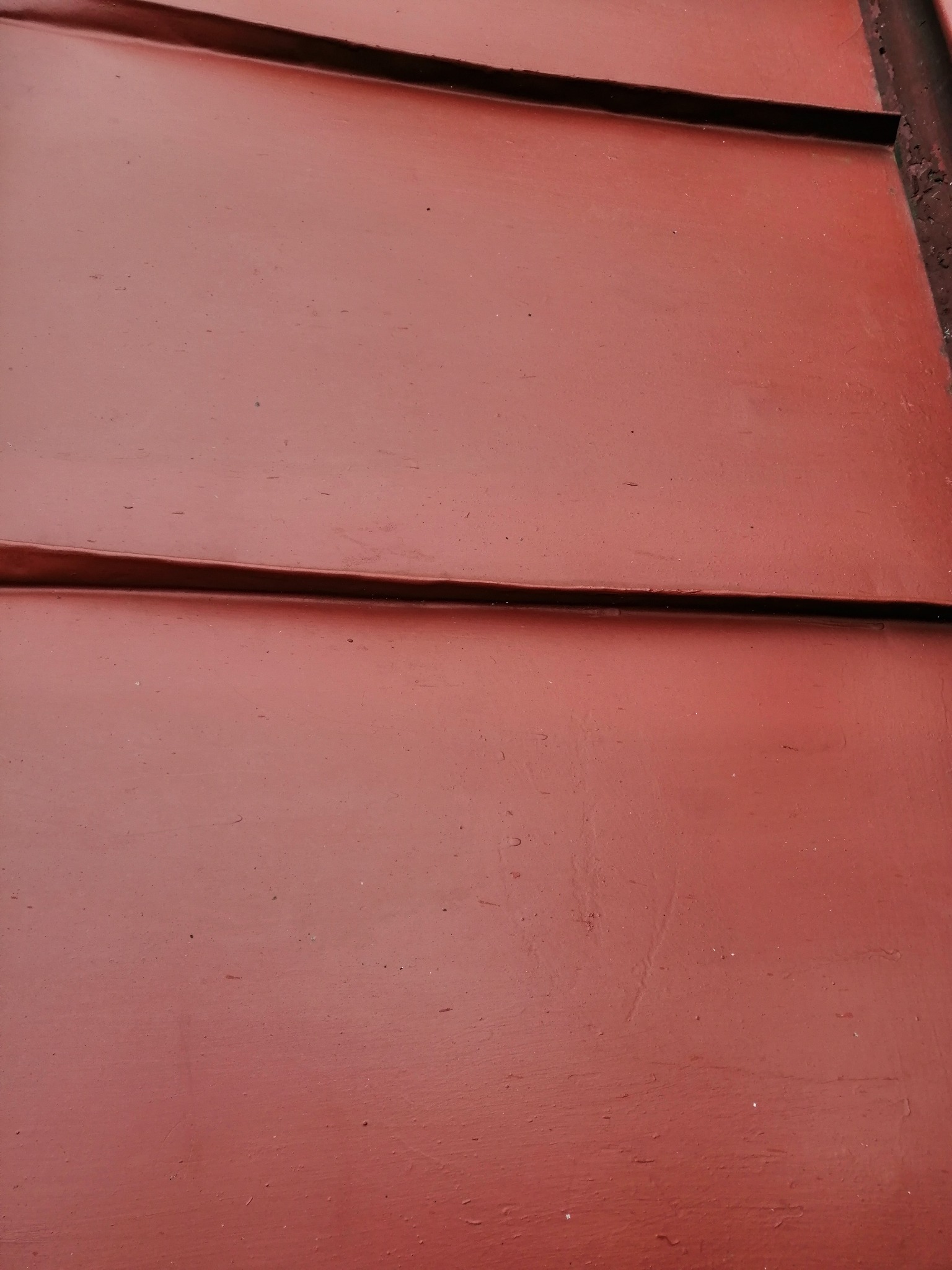 Czerwona, metalowa powierzchnia z widocznymi łączeniami paneli, prawdopodobnie po procesie czyszczenia lub malowania.