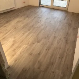 Ułożone panele podłogowe w jasnym odcieniu drewna, widok z góry na nową podłogę w pustym pokoju z dużym oknem balkonowym.