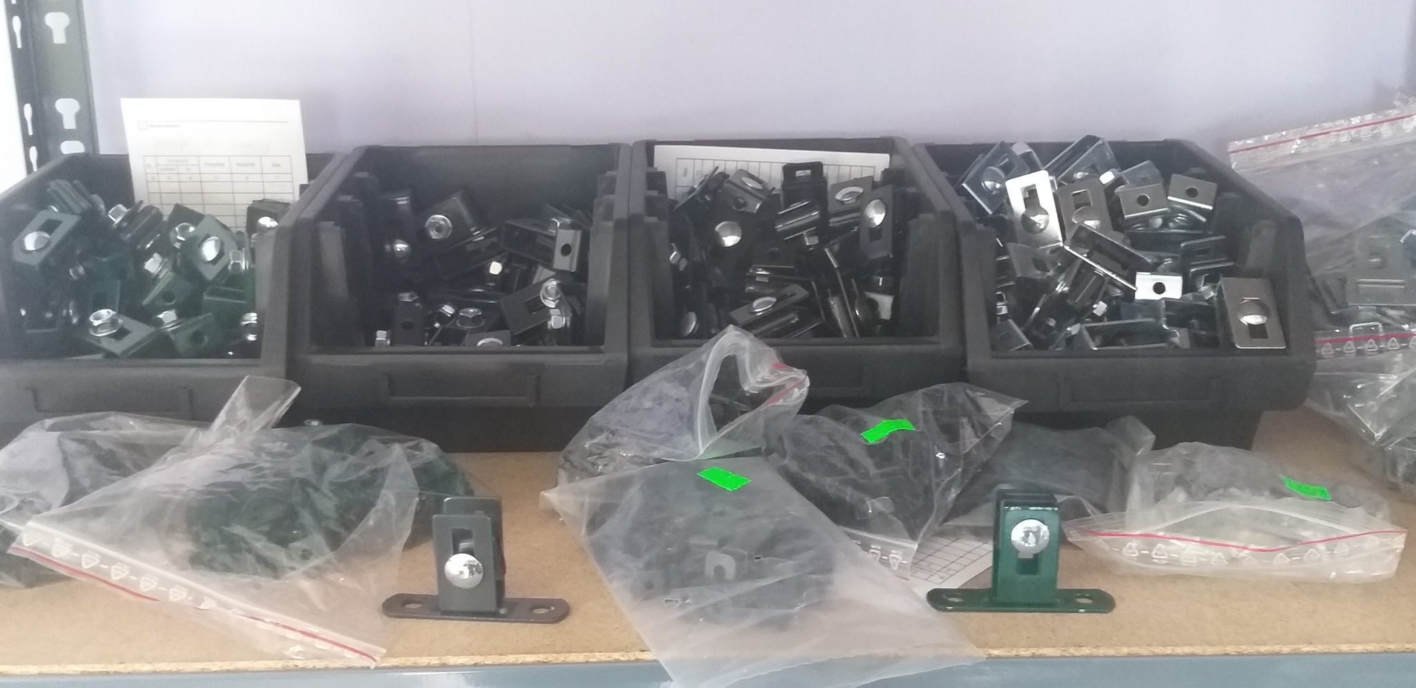 Elementy mocujące do ogrodzeń panelowych w pojemnikach i woreczkach foliowych, różne kolory i wykończenia.