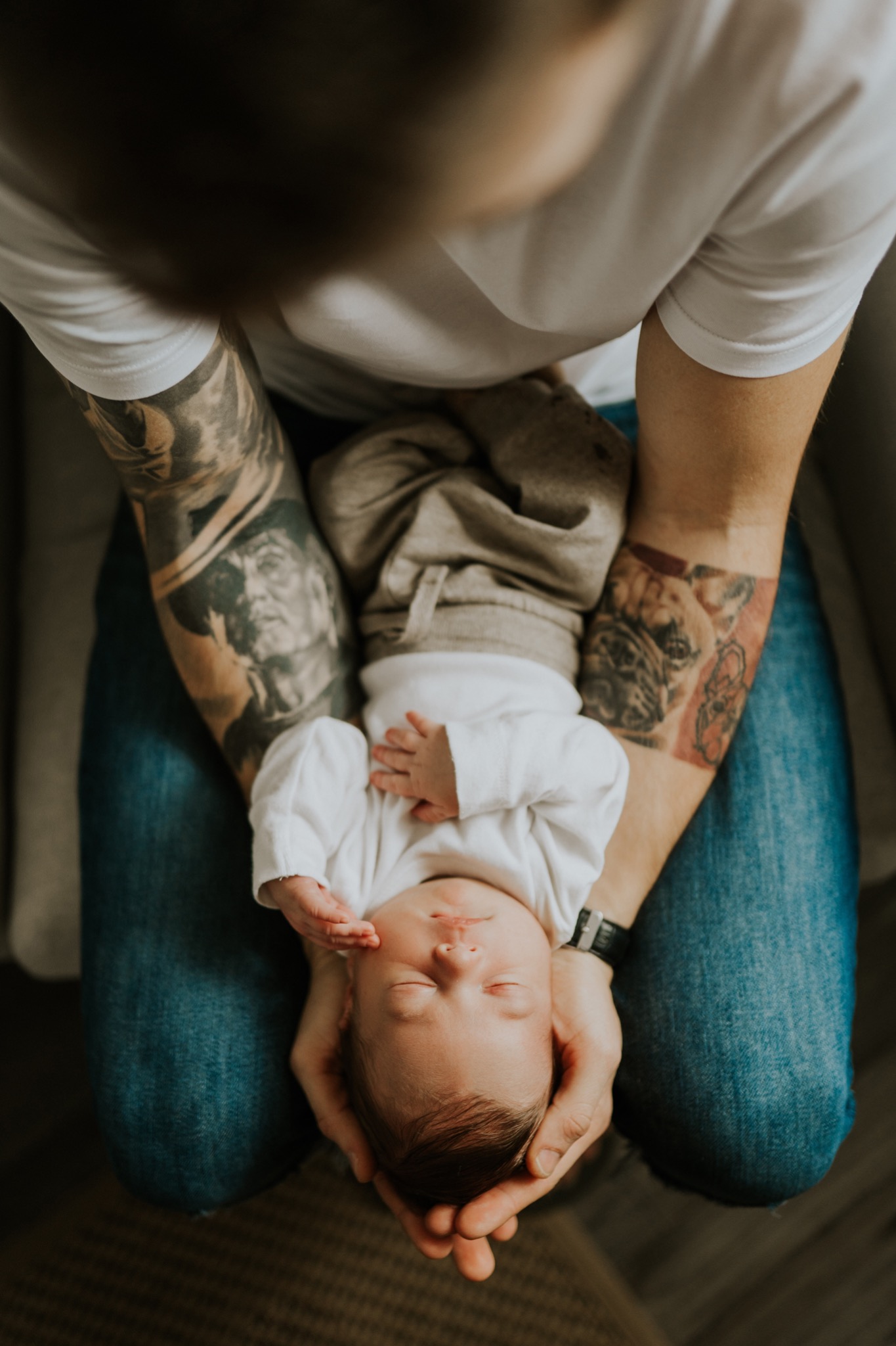 Noworodek śpiący w ramionach wytatuowanego taty we Wrocławiu, ujęcie z góry, spokojna atmosfera.