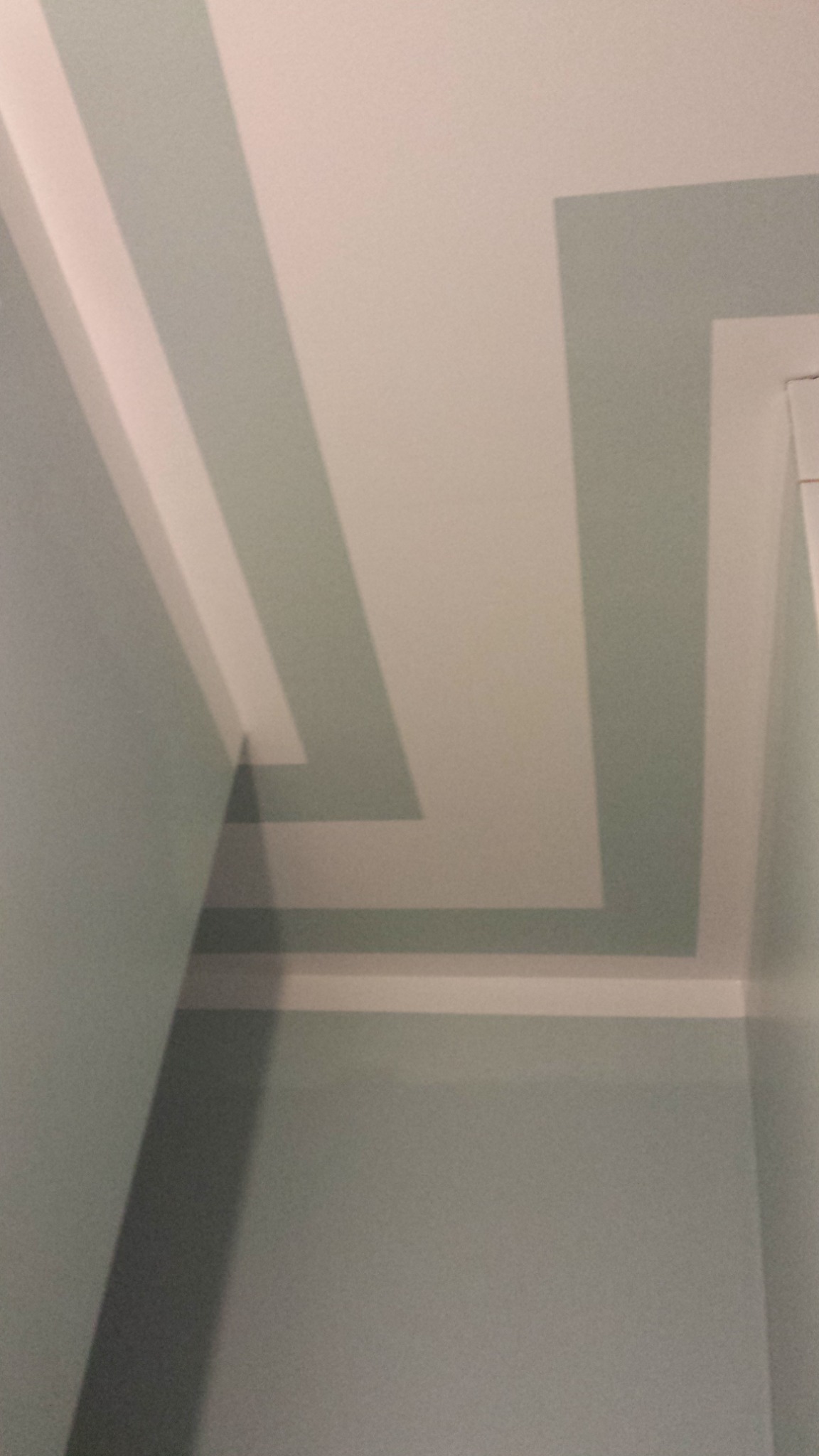 Fragment ściany i sufitu z geometrycznym wzorem w odcieniach bieli i błękitu, z widocznym fragmentem białej listwy przysufitowej.