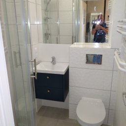Usługi Remontowo Budowlane - Nowoczesna łazienka po remoncie z kabiną prysznicową, umywalką z szafką w kolorze granatowym i toaletą. W lustrze odbija się osoba robiąca zdjęcie.