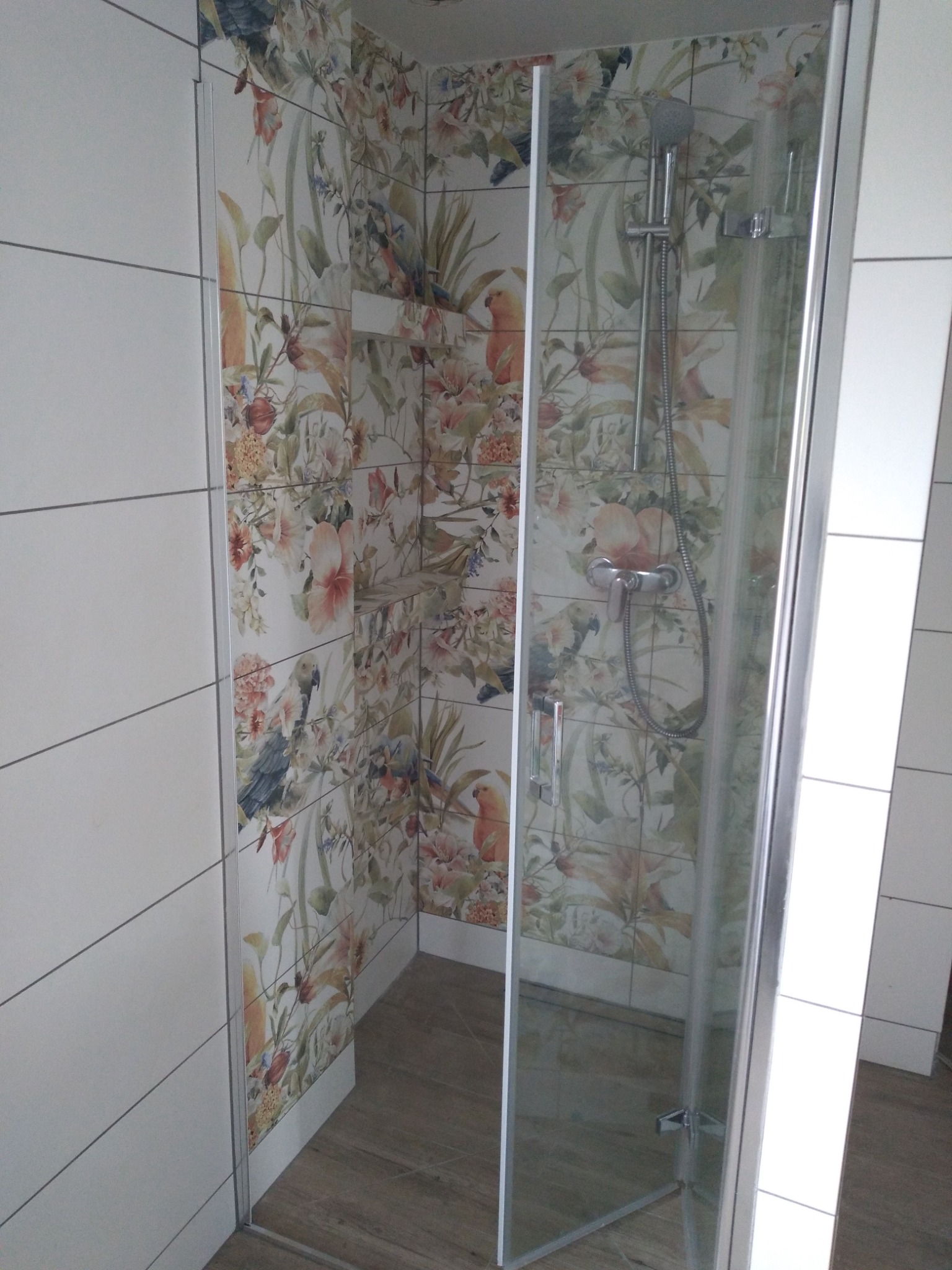 Kabina prysznicowa z motywem kwiatowym i ptasim w Białymstoku, widok z zewnątrz, brązowa podłoga, białe płytki po bokach.