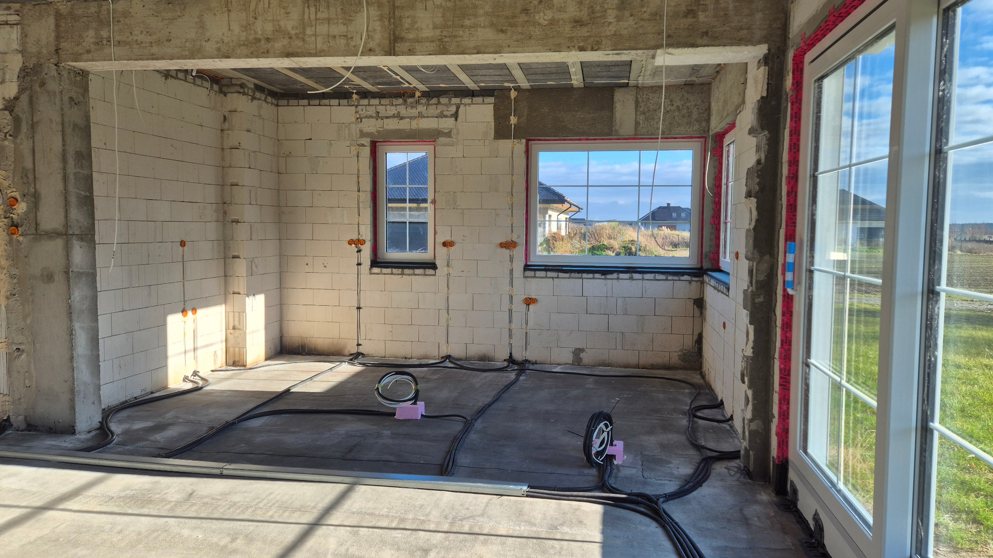 Surowy stan: instalacja elektryczna w domu jednorodzinnym. Widoczne kable w peszlach na podłodze i pomarańczowe puszki elektryczne w ścianach z betonu komórkowego.