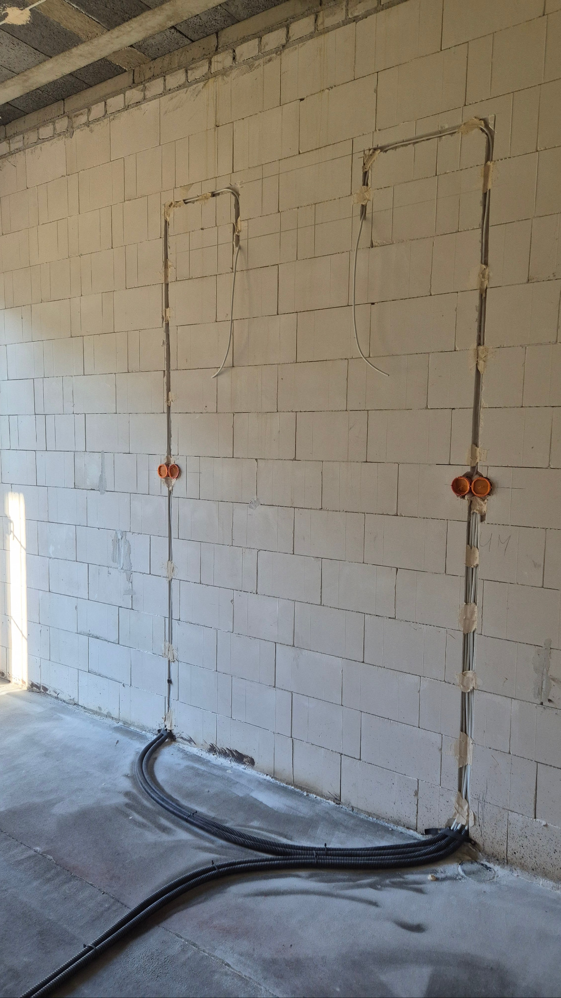 Wewnętrzna instalacja elektryczna w surowym budynku. Kable prowadzone w ścianach z bloczków, zabezpieczone taśmą. Rury karbowane na podłodze. Pomarańczowe puszki elektryczne.