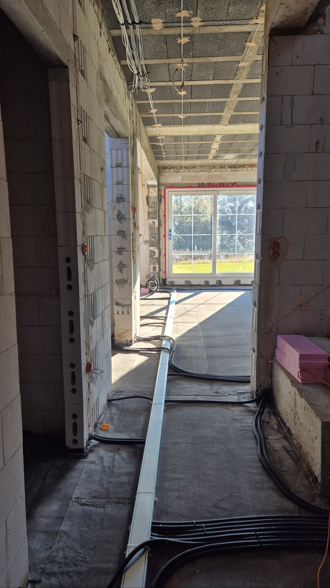 Wnętrze surowego budynku w trakcie prac. Widoczne kable elektryczne prowadzone po suficie i podłodze, puszki instalacyjne w ścianach z betonu komórkowego.