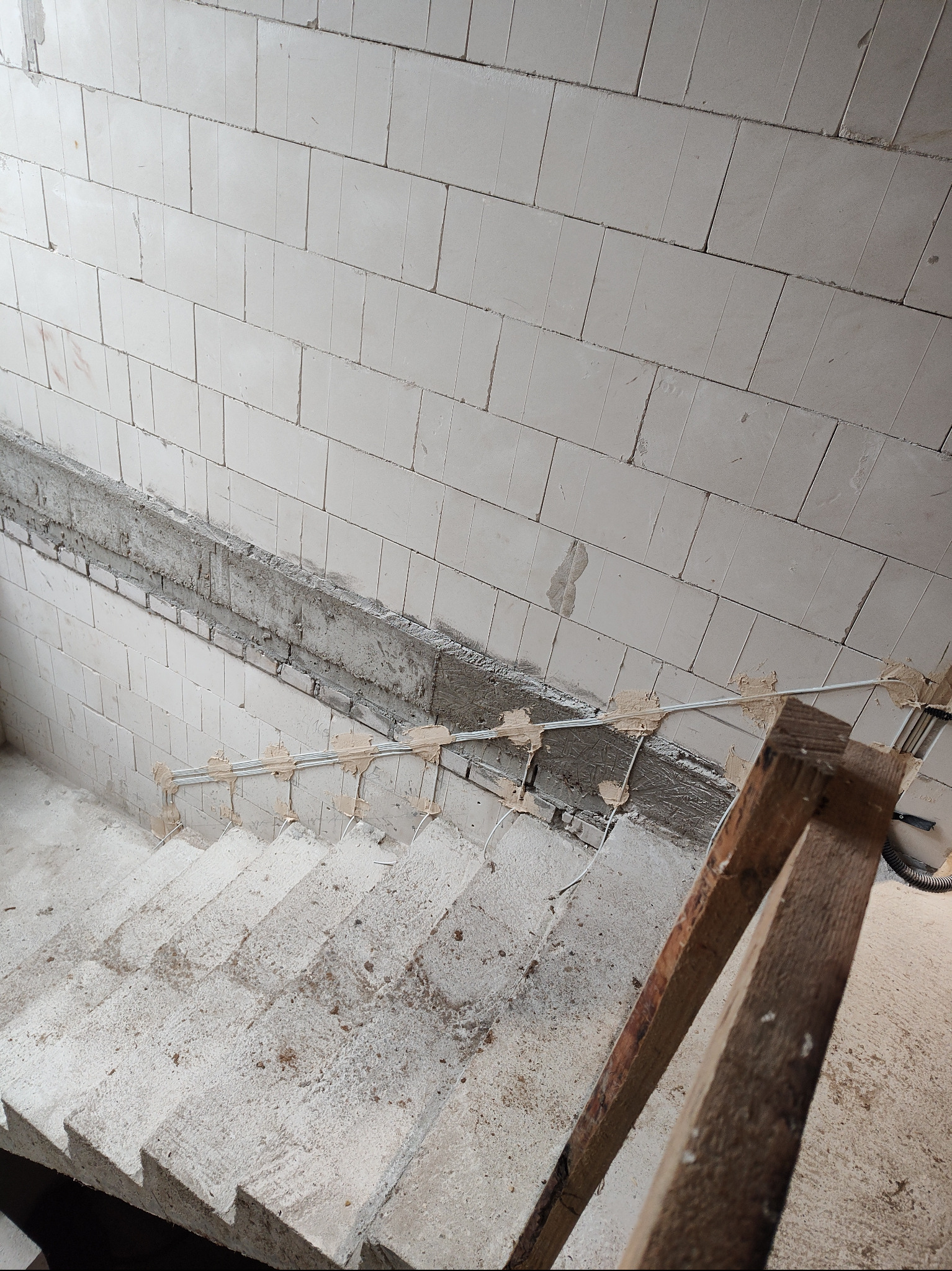 Surowe schody z białego betonu w trakcie montażu przewodów elektrycznych przy ścianie z pustaków. Widoczne kable przymocowane do ściany. Ujęcie z góry.