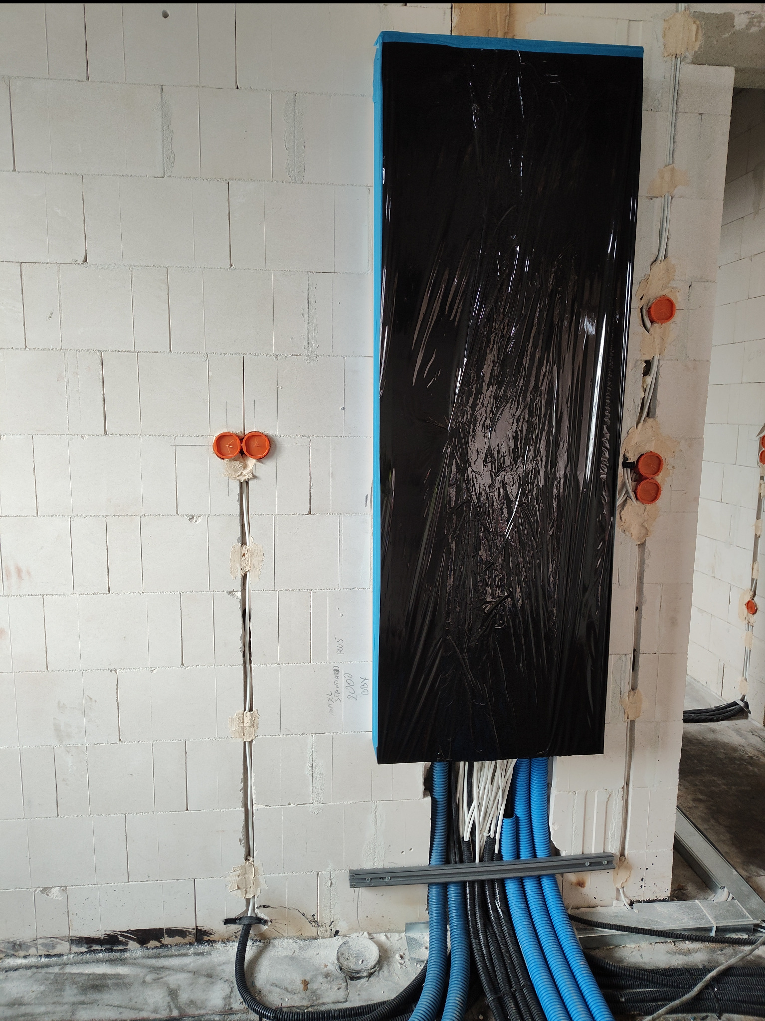Rozprowadzenie przewodów elektrycznych w ścianie z betonu komórkowego. Widoczne peszle w kolorze niebieskim i czarnym oraz puszki instalacyjne w kolorze pomarańczowym.
