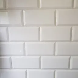 Białe, prostokątne, błyszczące płytki ułożone w rzędach, fuga w kolorze zbliżonym do płytek, widoczne delikatne odbicia światła.