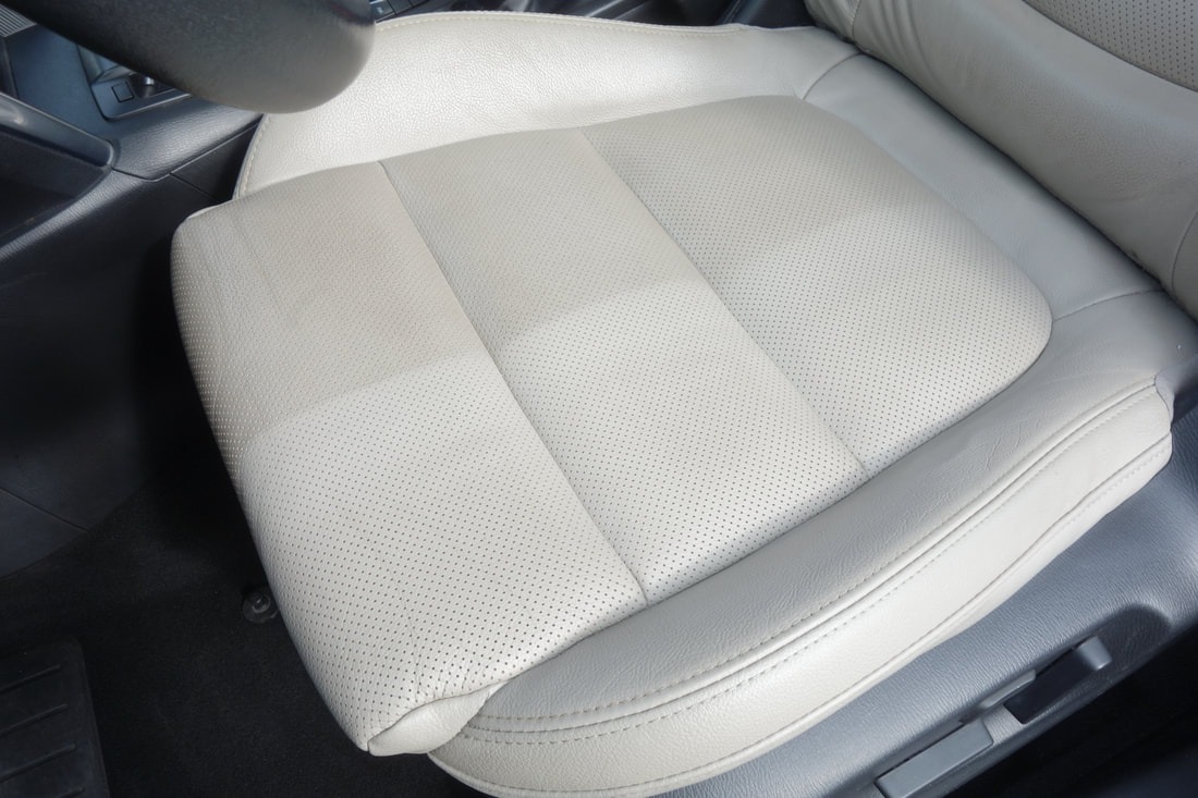 Jasny, perforowany skórzany fotel samochodowy, widoczna wyraźna różnica w czystości między częścią wyczyszczoną a nieczyszczoną.