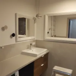 Nowoczesna łazienka po remoncie: biała umywalka nablatowa, drewniana szafka, dwa lustra w białych ramach i minimalistyczna lampa wisząca.