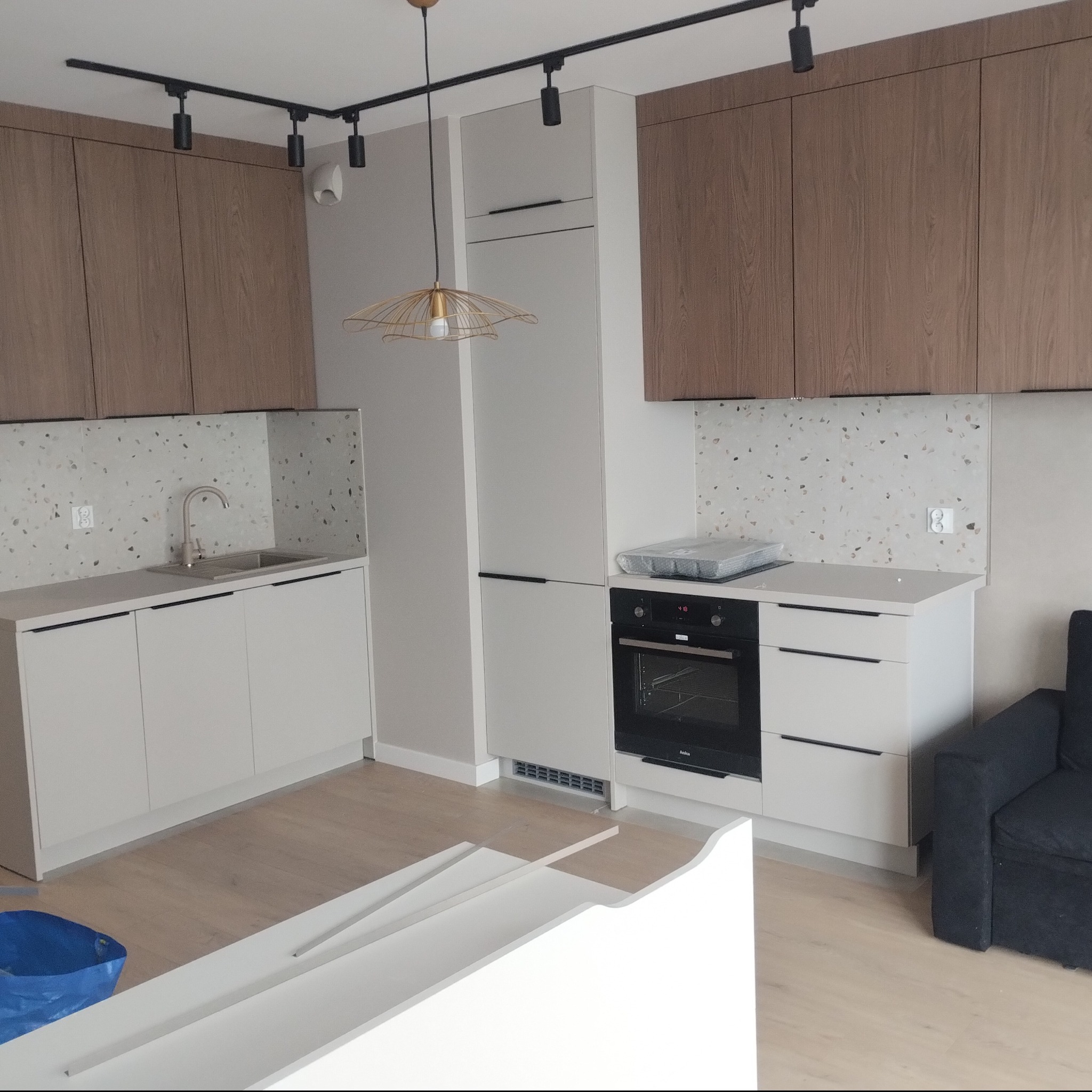 Nowoczesna kuchnia z zabudową w odcieniach bieli i drewna, z lampą wiszącą. Wykończenie wnętrz w Stargardzie z dbałością o detale i funkcjonalność.