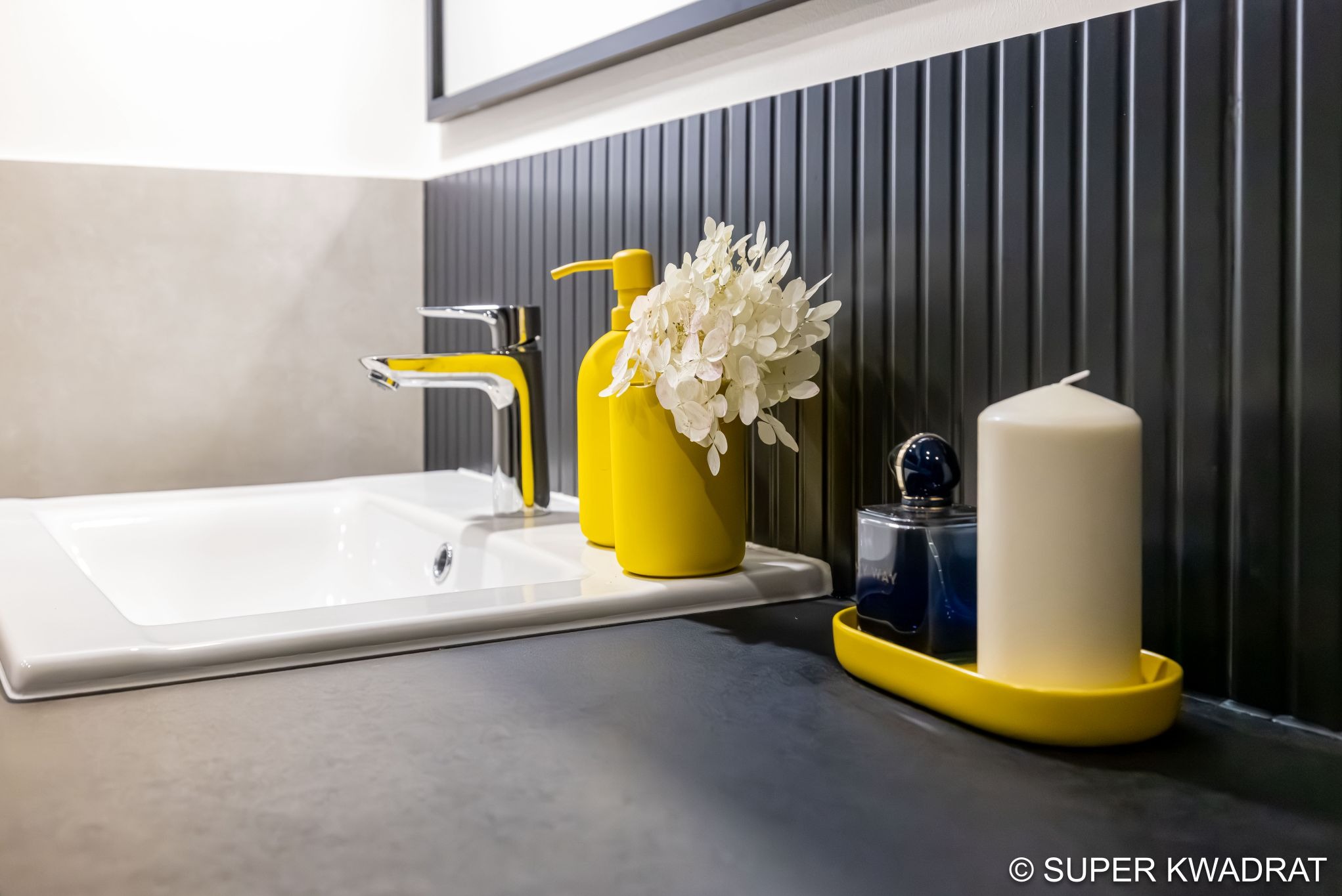 Nowoczesna łazienka: biała umywalka z chromowaną baterią z żółtymi akcentami, czarne panele ścienne, żółte akcesoria i kwiaty. Stylowe wykończenie wnętrza.