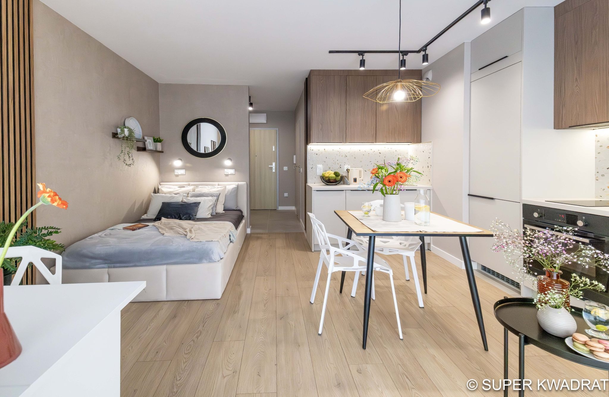 Nowoczesne studio: łóżko z wezgłowiem, stół z krzesłami, aneks kuchenny z oświetleniem punktowym. Drewniane panele ścienne i podłoga. Minimalistyczny design.