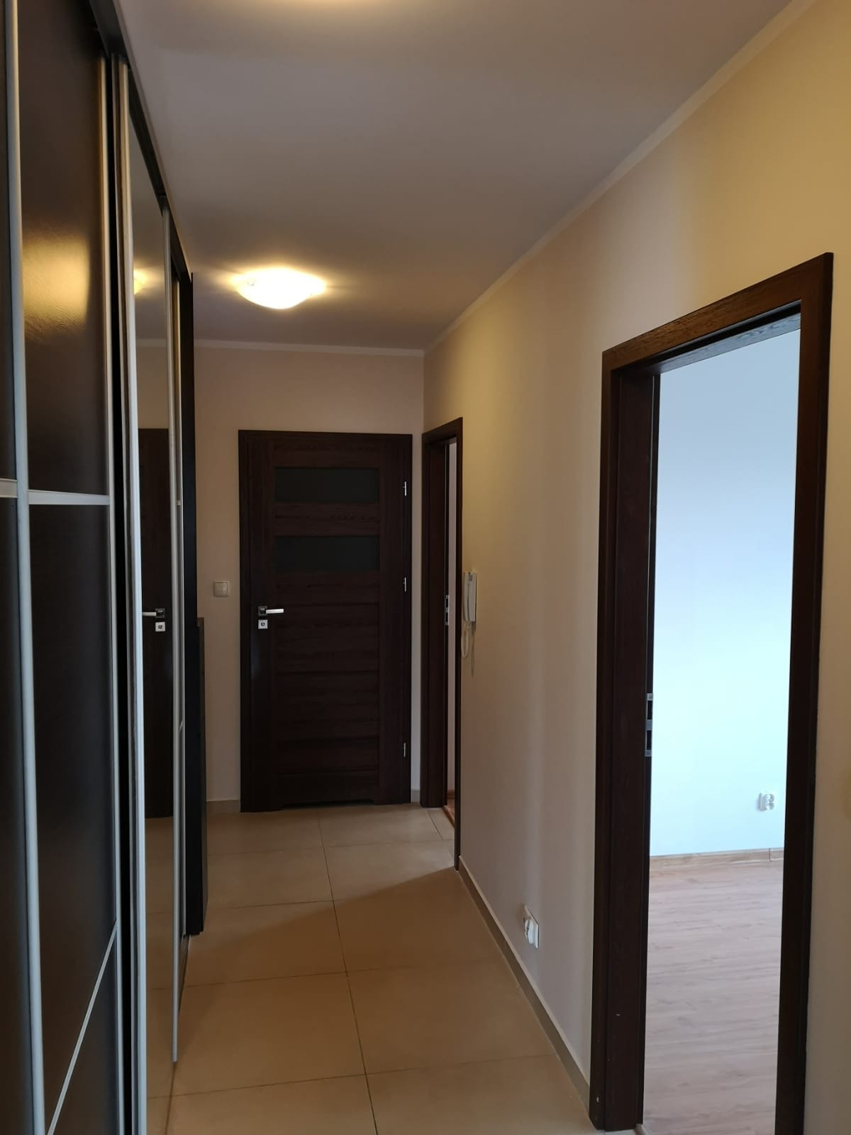 Korytarz w mieszkaniu po remoncie: ściany w odcieniach beżu, ciemne drewniane drzwi i szafa z lustrami, jasna podłoga z płytek.