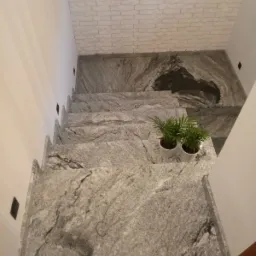 Granitowe schody wewnętrzne z doniczkami z zielonymi roślinami na jednym ze stopni, widok z góry, ściana z dekoracyjnej cegły.