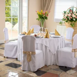Elegancko nakryty stół z białym obrusem, złotymi serwetkami i kwiatami w wazonie i koszu, przygotowany na uroczystość w Sali Warszkowski Młyn.