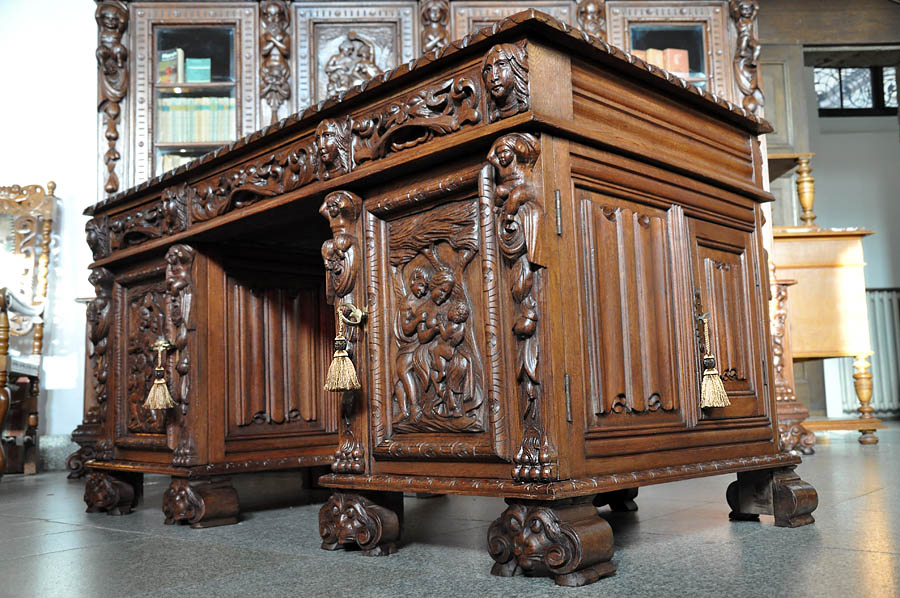 Bogato rzeźbiony, neorenesansowy komplet mebli gabinetowych z XVIII/XIX wieku, ukazujący detale figuralne i ornamentacyjne, z widocznym motywem rodziny na panelu bocznym i dekoracyjnymi frędzlami...