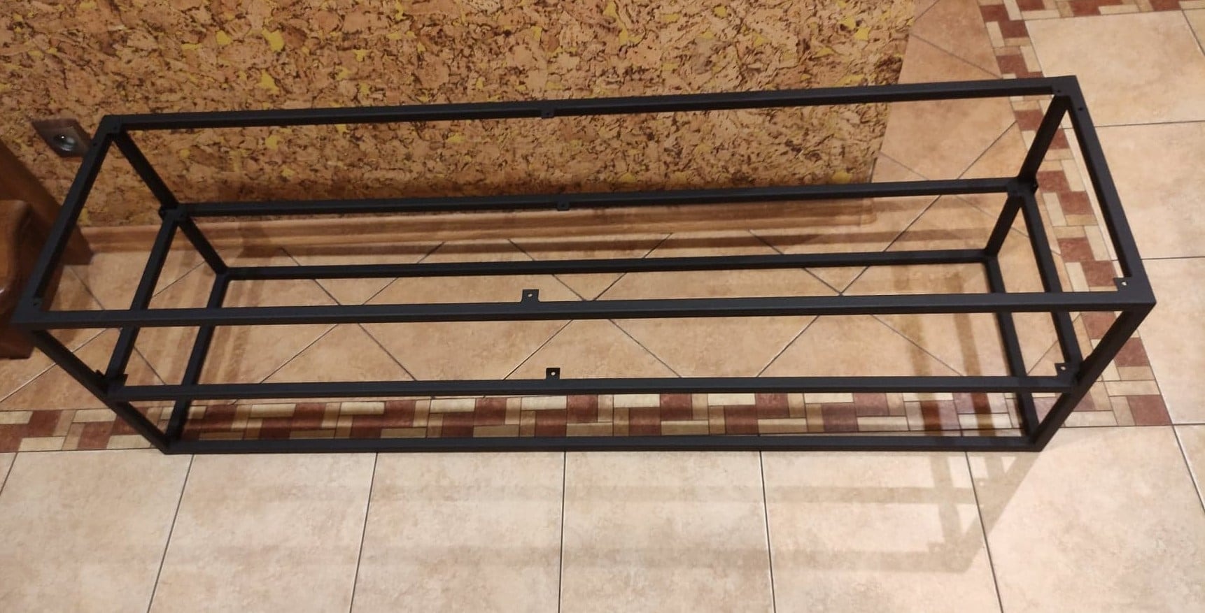 Spawana, czarna, prostokątna rama z profili stalowych, widoczne otwory montażowe na dwóch poprzeczkach, na podłodze z płytek ceramicznych.