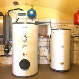 ML ENERGY SP. Z O.O. - Instalacja dwóch białych zbiorników buforowych Nesheat z osprzętem, widoczny także szary piec, instalacja elektryczna i pralka w pomieszczeniu wyłożonym kafelkami.